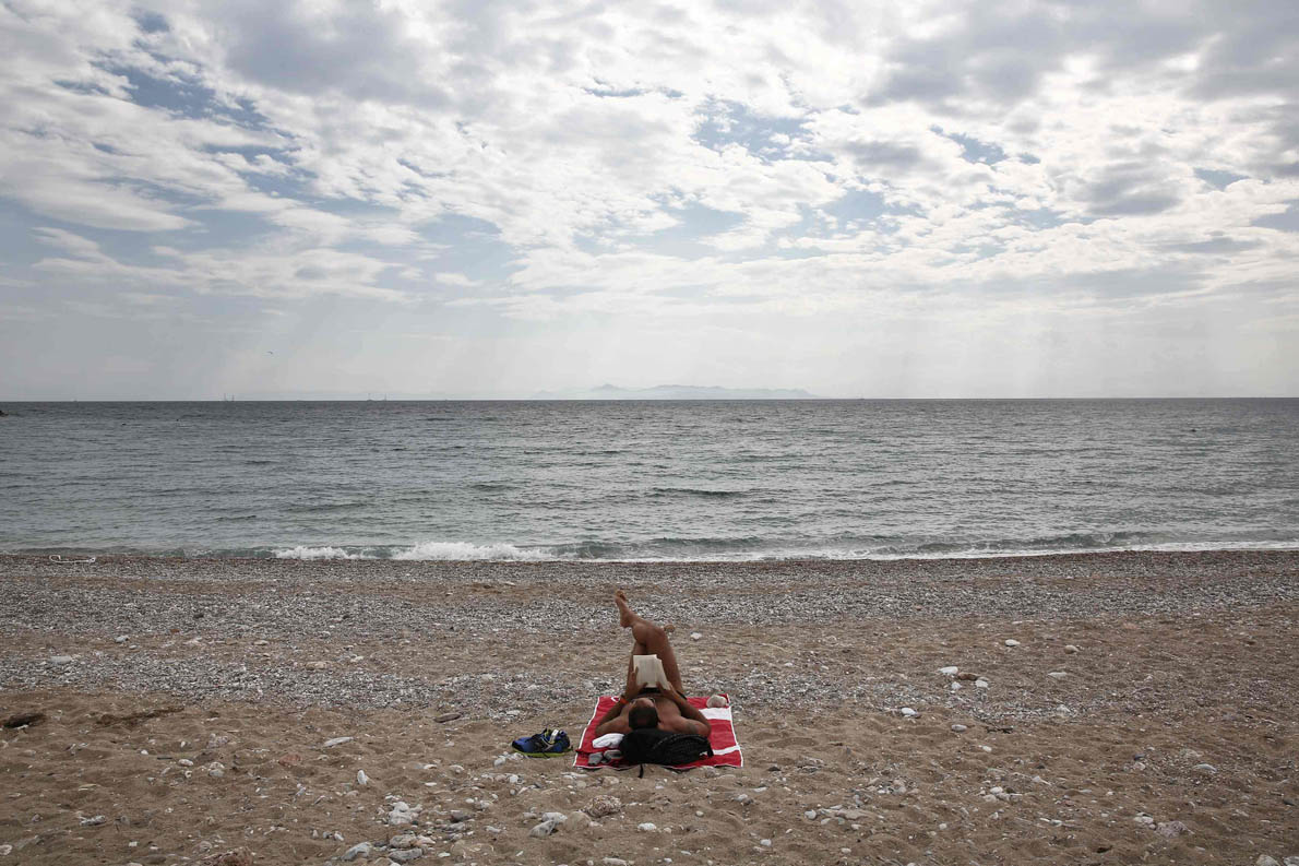 A man reads a book at a beach in Glyfada, a suburb southeast of Athens May 10, 2014. Greece's plan to allow more construction and business activity along its vast Mediterranean coastline to boost its economy has sparked uproar in a country whose pristine beaches attract millions of tourists each year. Greece's long coastline remains less developed than other Southern Europe peers like Spain and a draft bill proposes swifter permits for beachside hotels and eases restrictions on setting up umbrellas, drink stands and sun beds. Picture taken on May 10, 2014. REUTERS/Yorgos Karahalis (GREECE - Tags: POLITICS BUSINESS TRAVEL)