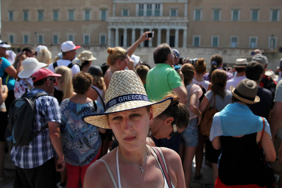 A woman looks on while tourists watch a ceremonial parade in front of the parliament building in Athens, Greece July 26, 2015. Greek banks are set to keep broad cash controls in place for months, until fresh money arrives from Europe and with it a sweeping restructuring, officials believe.  REUTERS/ Yiannis Kourtoglou